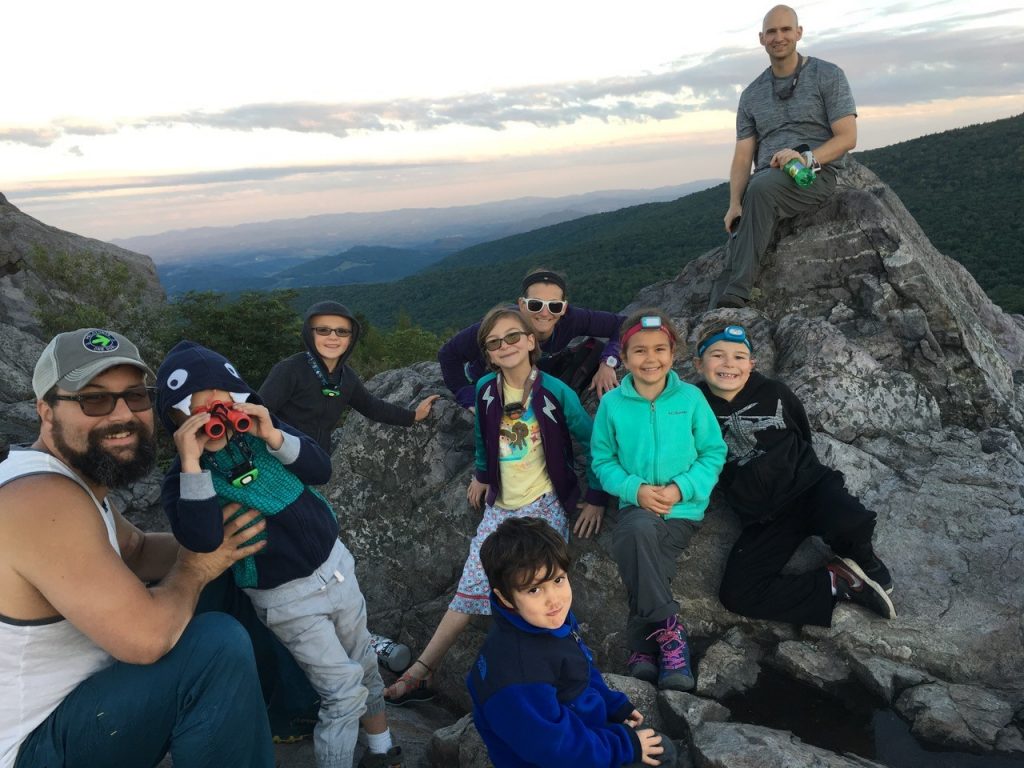 A family sitting together on top of an outdoor crag at sunset