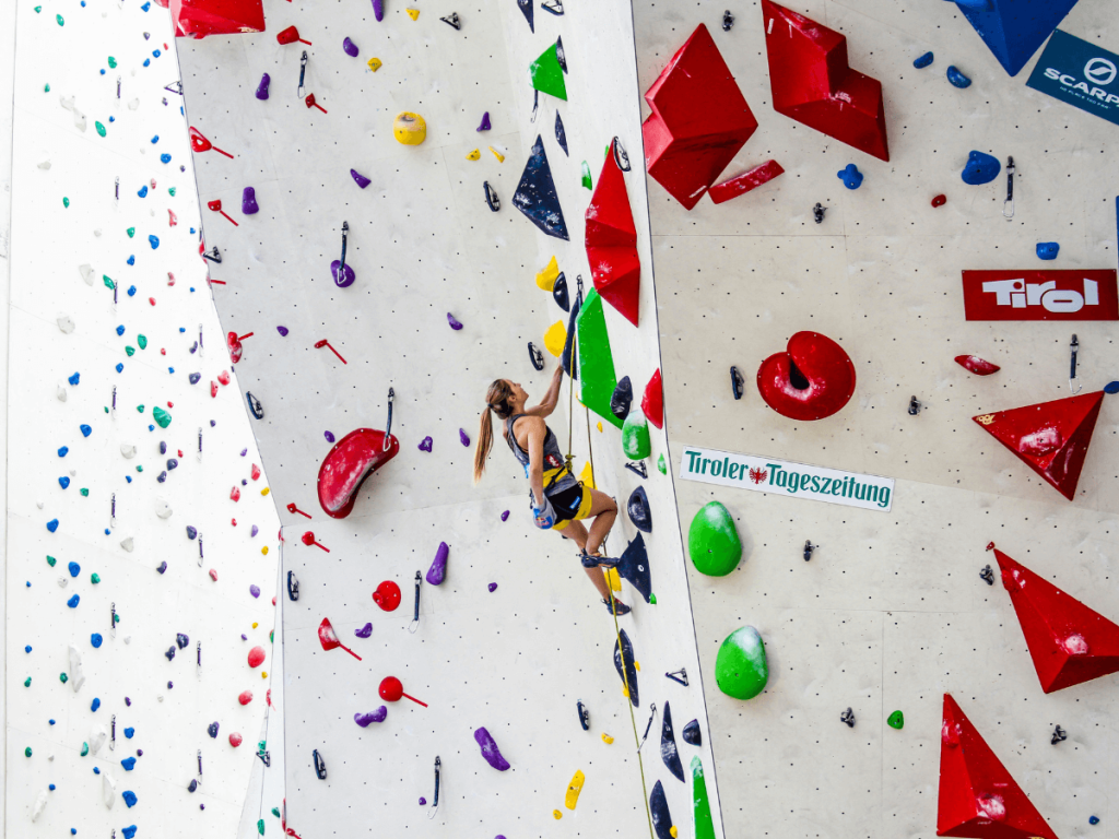 woman calimbing a climbing wall with colorful climbing holds