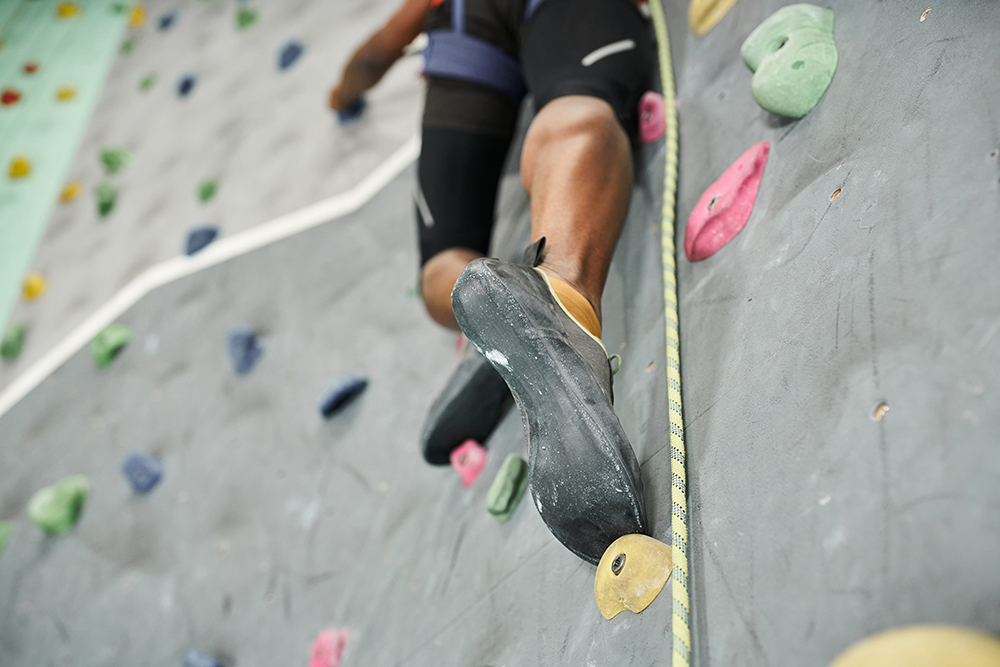 cropped view of legs of sporty man climbing up rock wall with safety rope